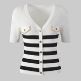 White cardigan with black and white striped pattern and gold buttons on a gray background