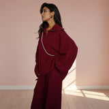 Woman wearing a burgundy outfit with a pearl necklace on a plain background