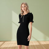 Woman wearing a black dress with ruffled sleeves against a light green wall.