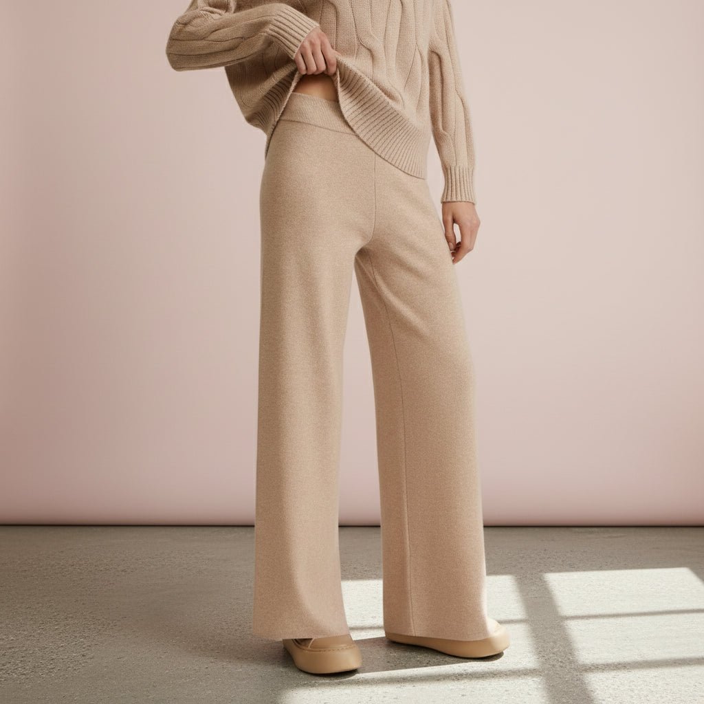 Person wearing a beige sweater and wide-leg pants against a pink wall.