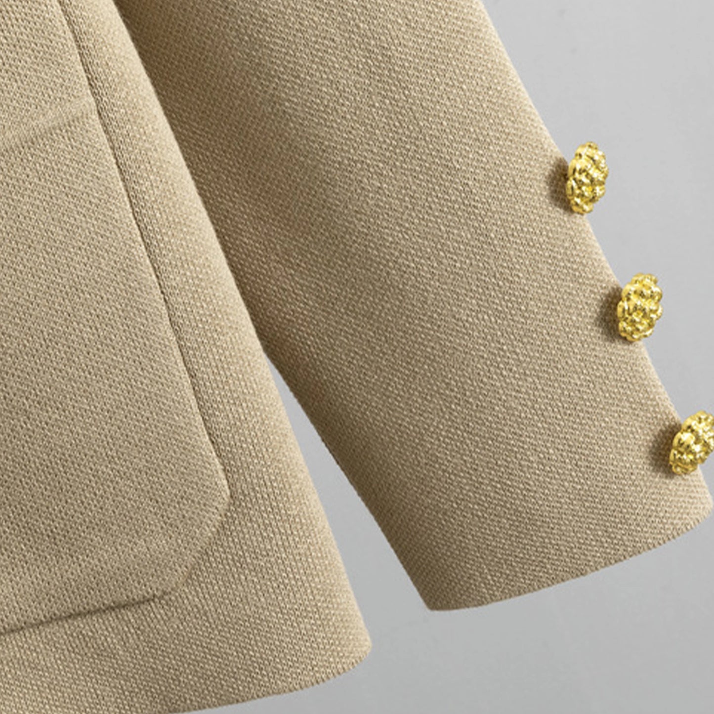 Close-up of a beige textured fabric with gold buttons on a gray background