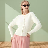 Woman wearing a white cardigan and pink pants against a light green wall.