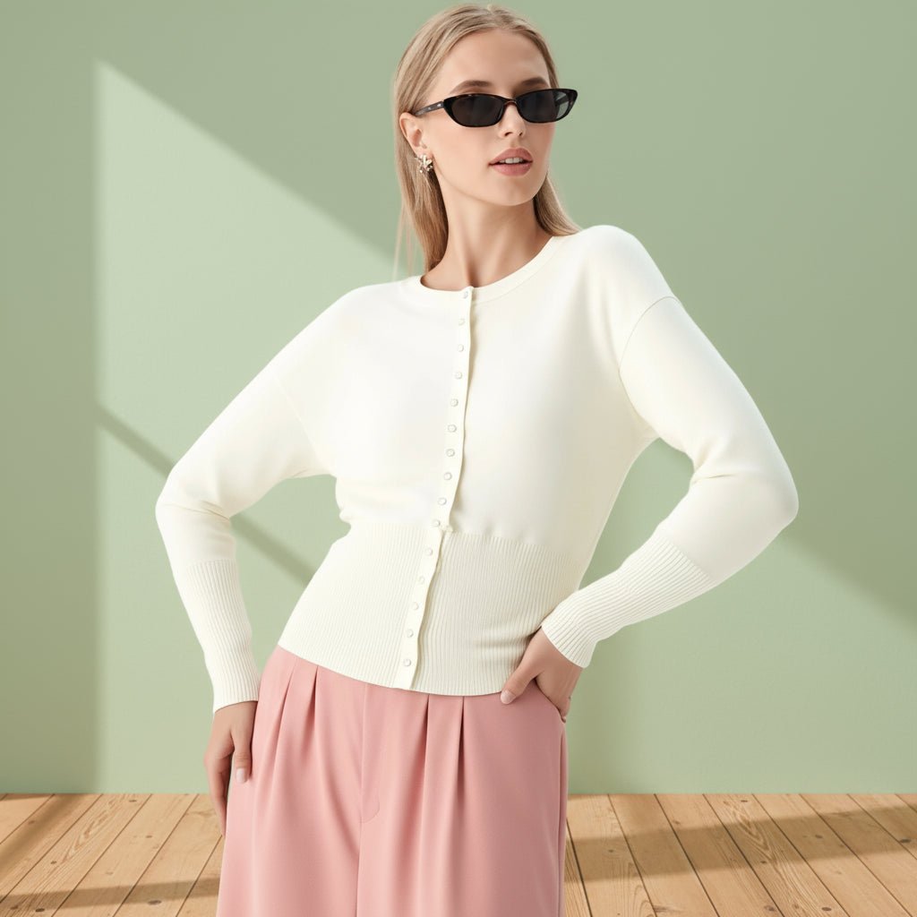 Woman wearing a white cardigan and pink pants against a light green wall.