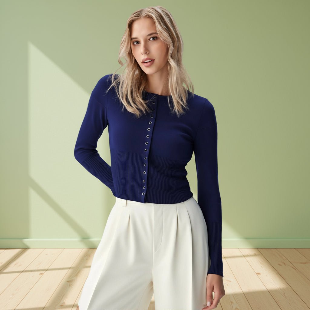 Woman wearing a blue cardigan and white pants against a light green wall.