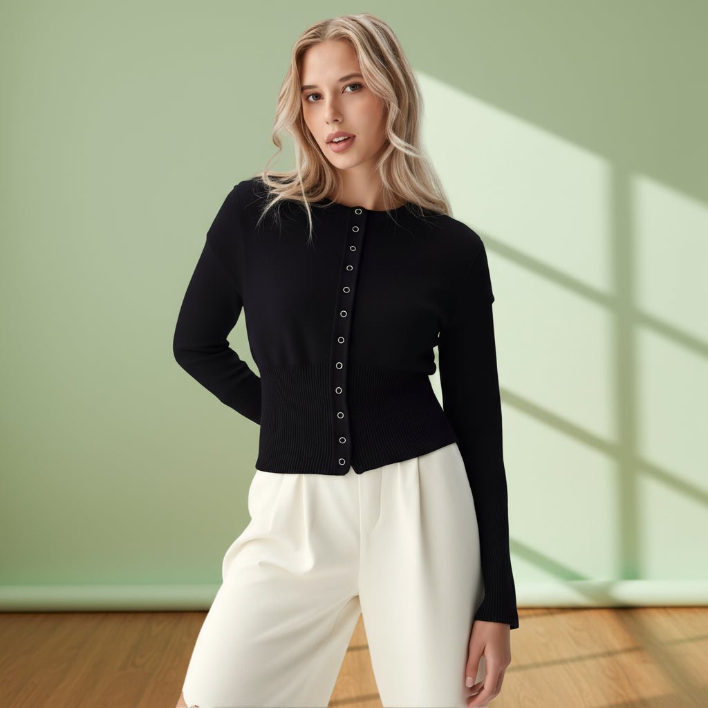 Woman wearing a black cardigan and white pants against a light green wall.