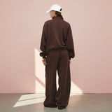 Person wearing a brown tracksuit and white cap against a pink wall