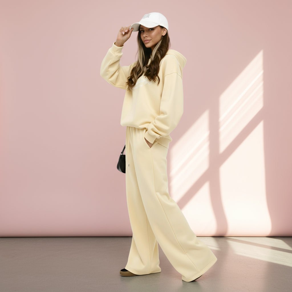 Woman in a light yellow outfit with a white cap against a pink wall.