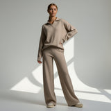 Woman wearing a beige sweater and pants standing against a neutral background
