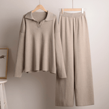 Beige long-sleeve shirt and pants set hanging on wooden hangers against a plain wall.