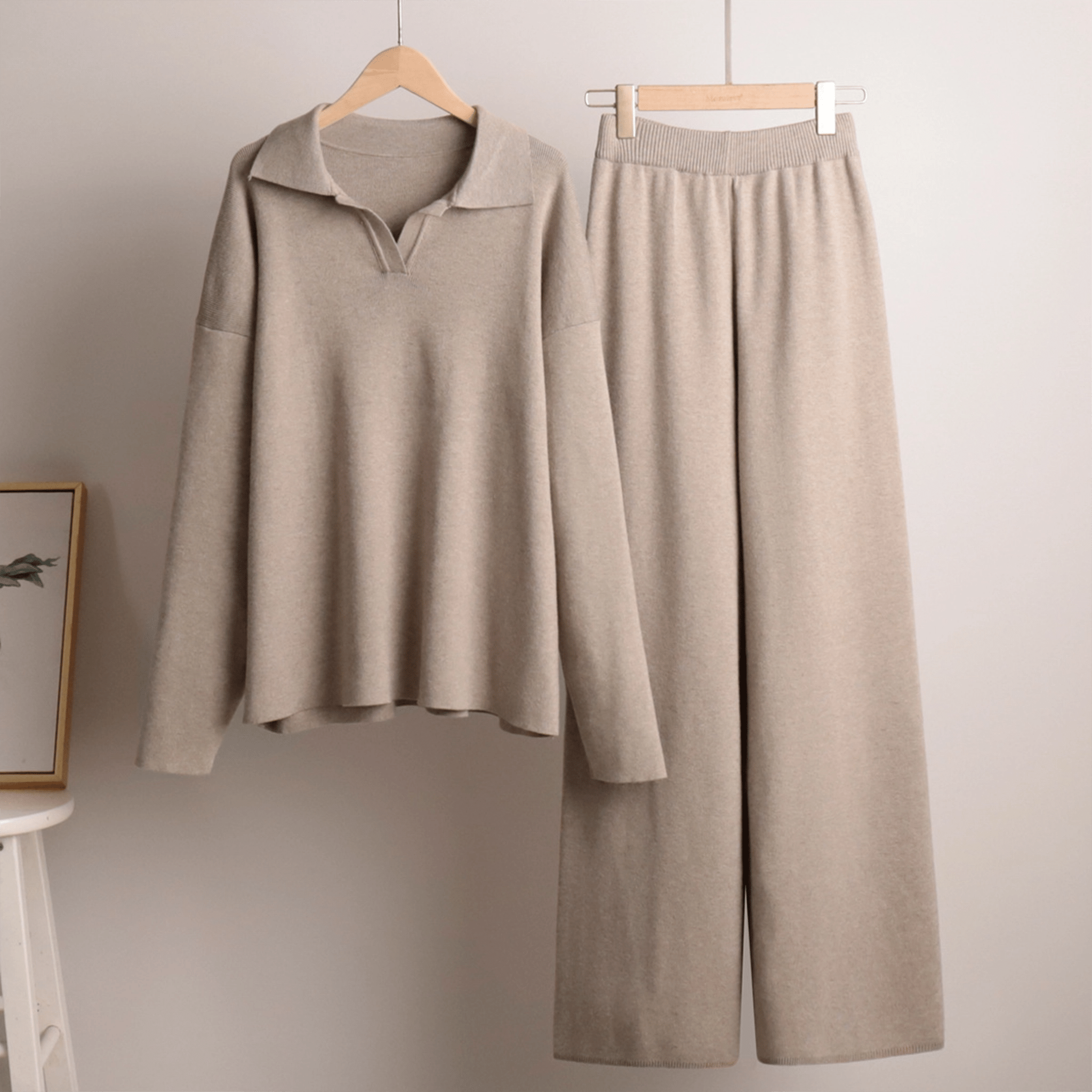 Beige long-sleeve shirt and pants set hanging on wooden hangers against a plain wall.