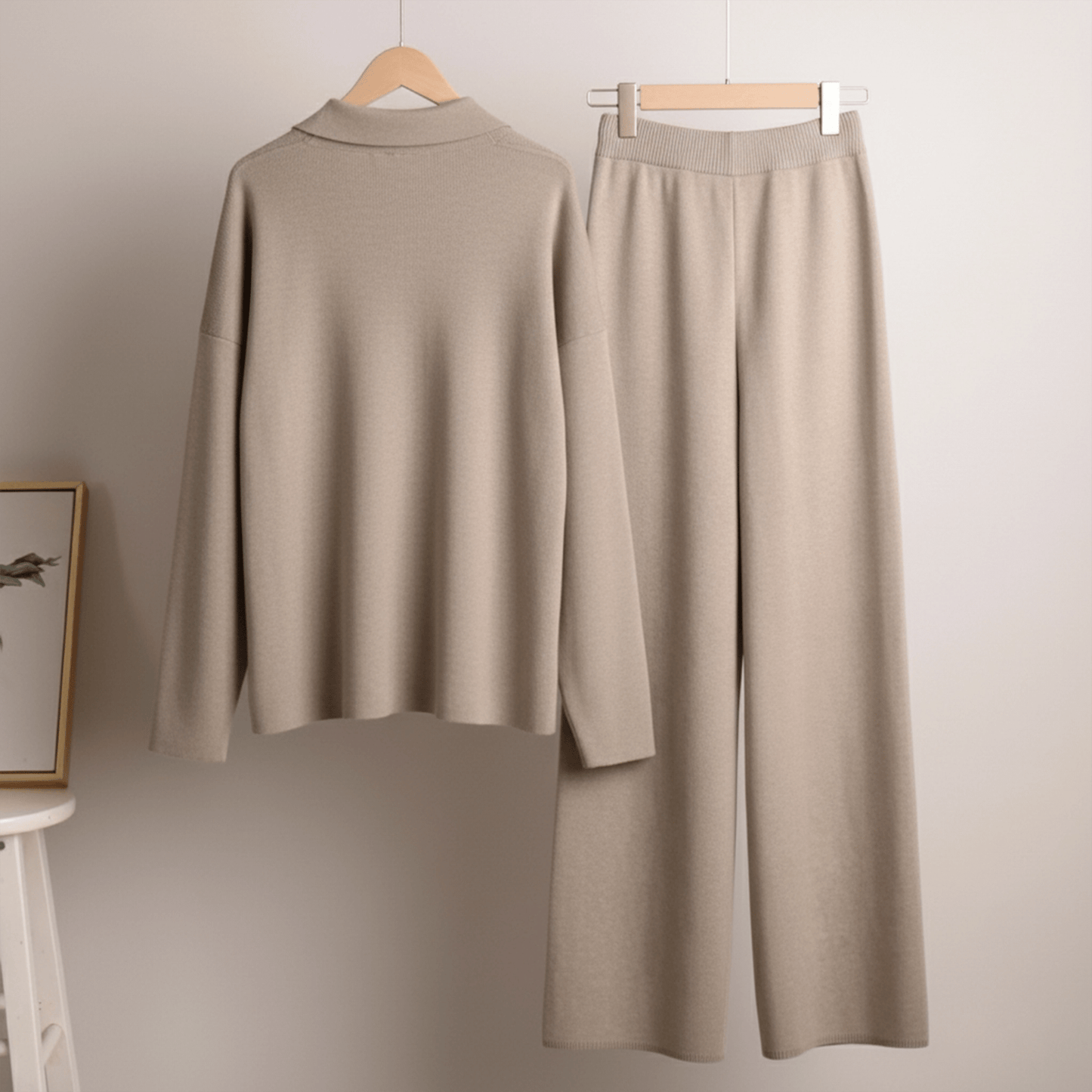 Beige long-sleeve top and wide-leg pants on hangers against a plain wall.