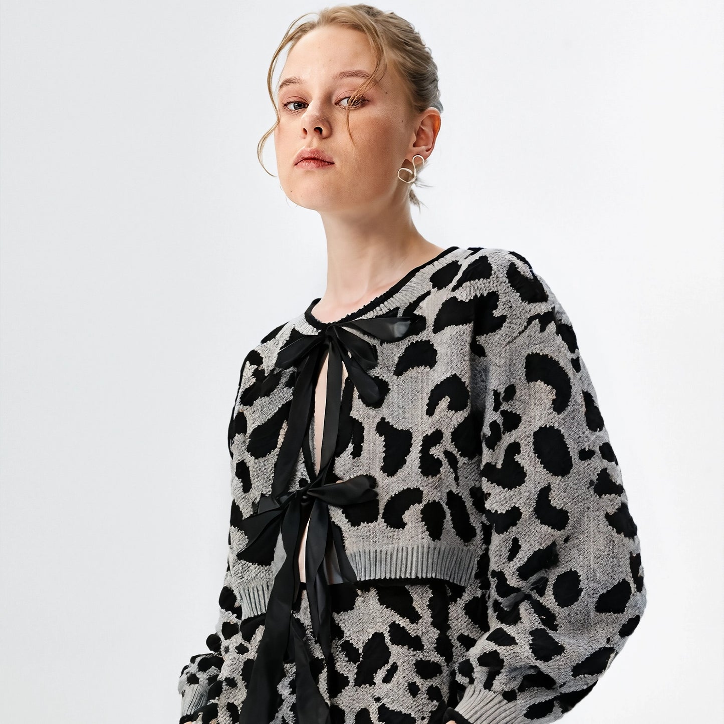 Person wearing a black and white patterned sweater with a bow tie on a light gray background