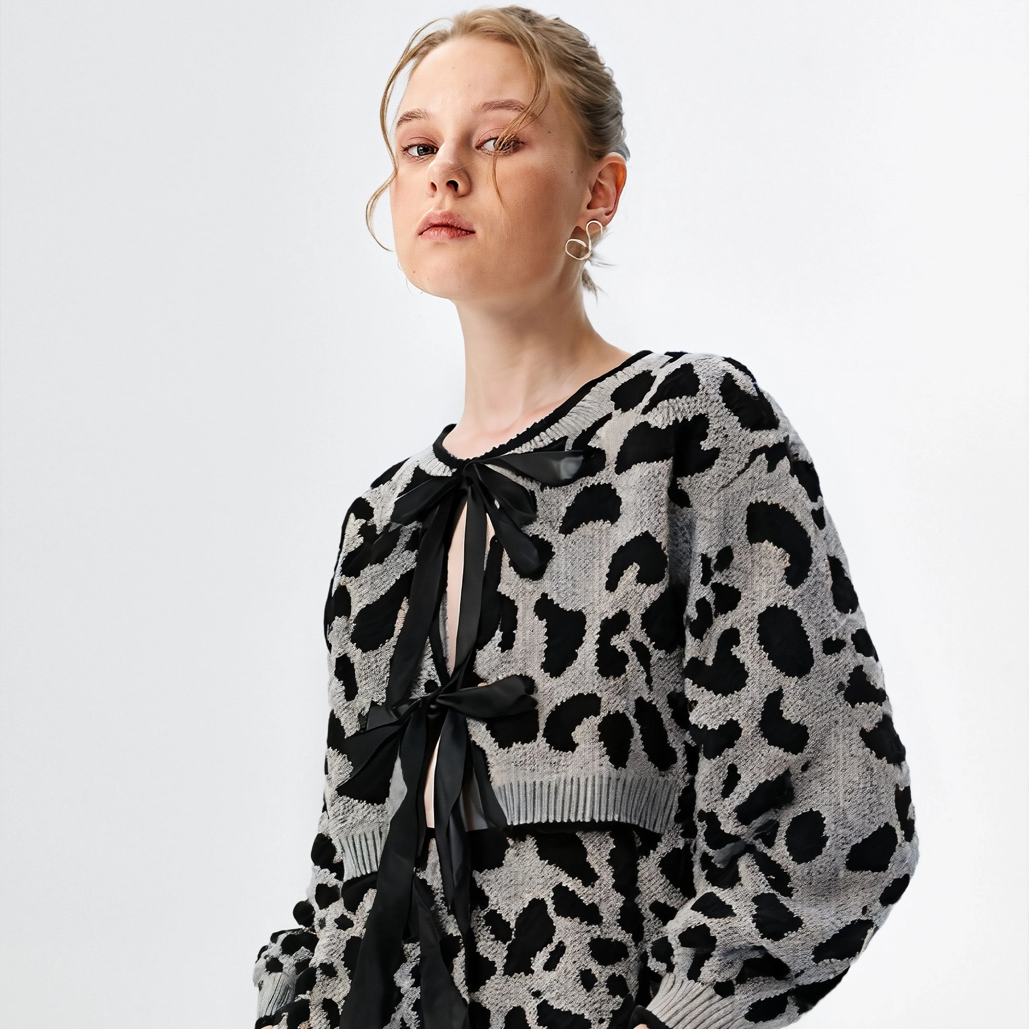 Person wearing a black and white patterned sweater with a bow tie on a light gray background