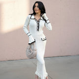 Woman in a white outfit with black accents standing against a light pink wall.