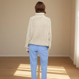 Person wearing a beige knitted sweater and light blue pants on a gray background