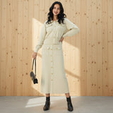 Woman wearing a beige coat holding a black handbag on a gray background