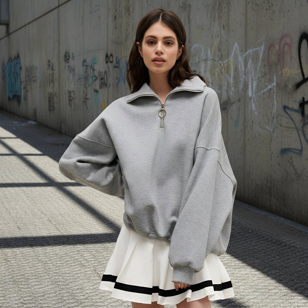 Woman wearing a gray oversized sweater over a white dress with black trim on a light gray background