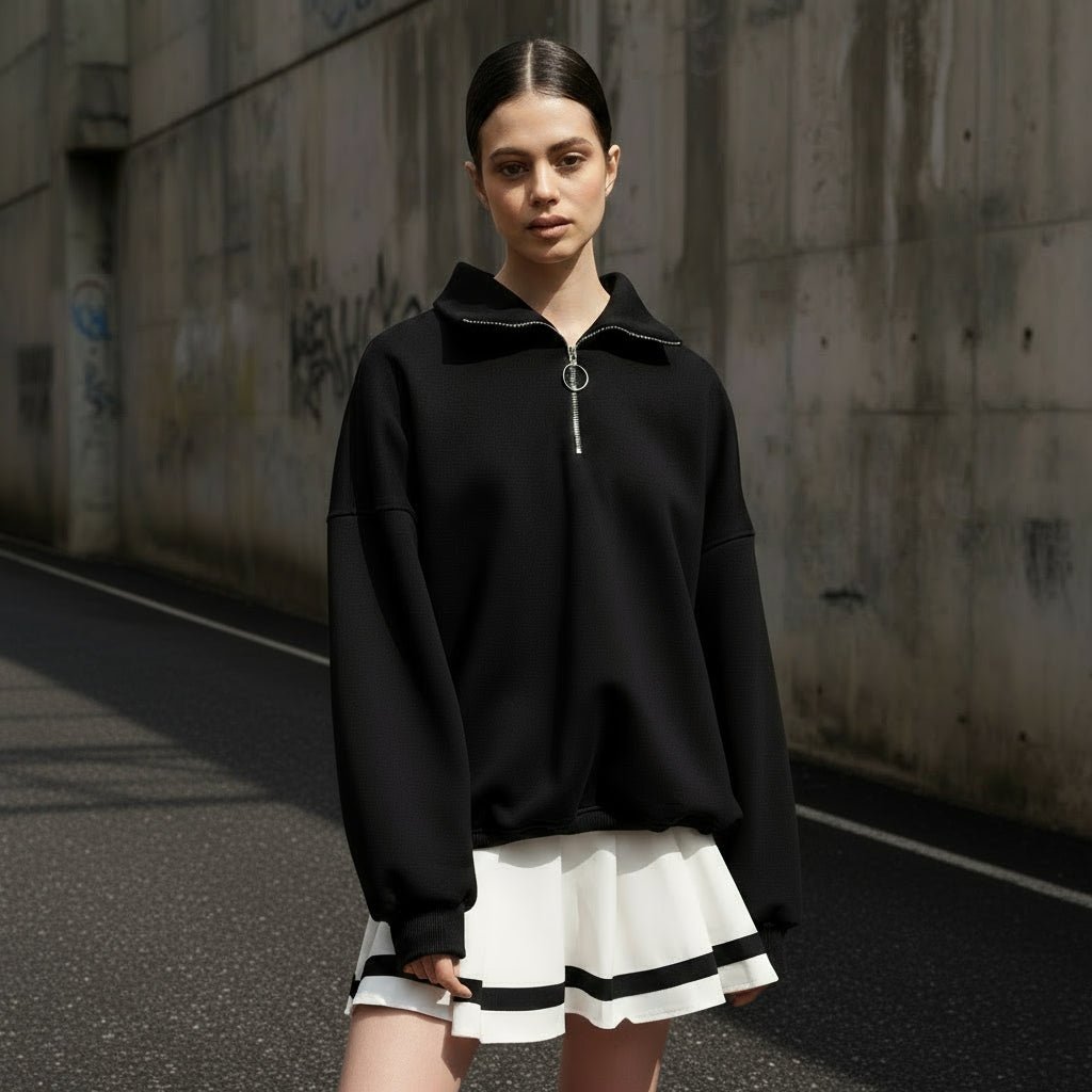 Person wearing a black zip-up sweatshirt with a white skirt on a light gray background