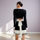 Woman wearing a black and white outfit with a tie detail against a light purple wall.