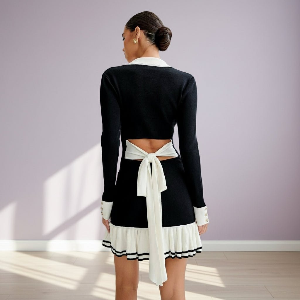 Woman wearing a black and white outfit with a tie detail against a light purple wall.