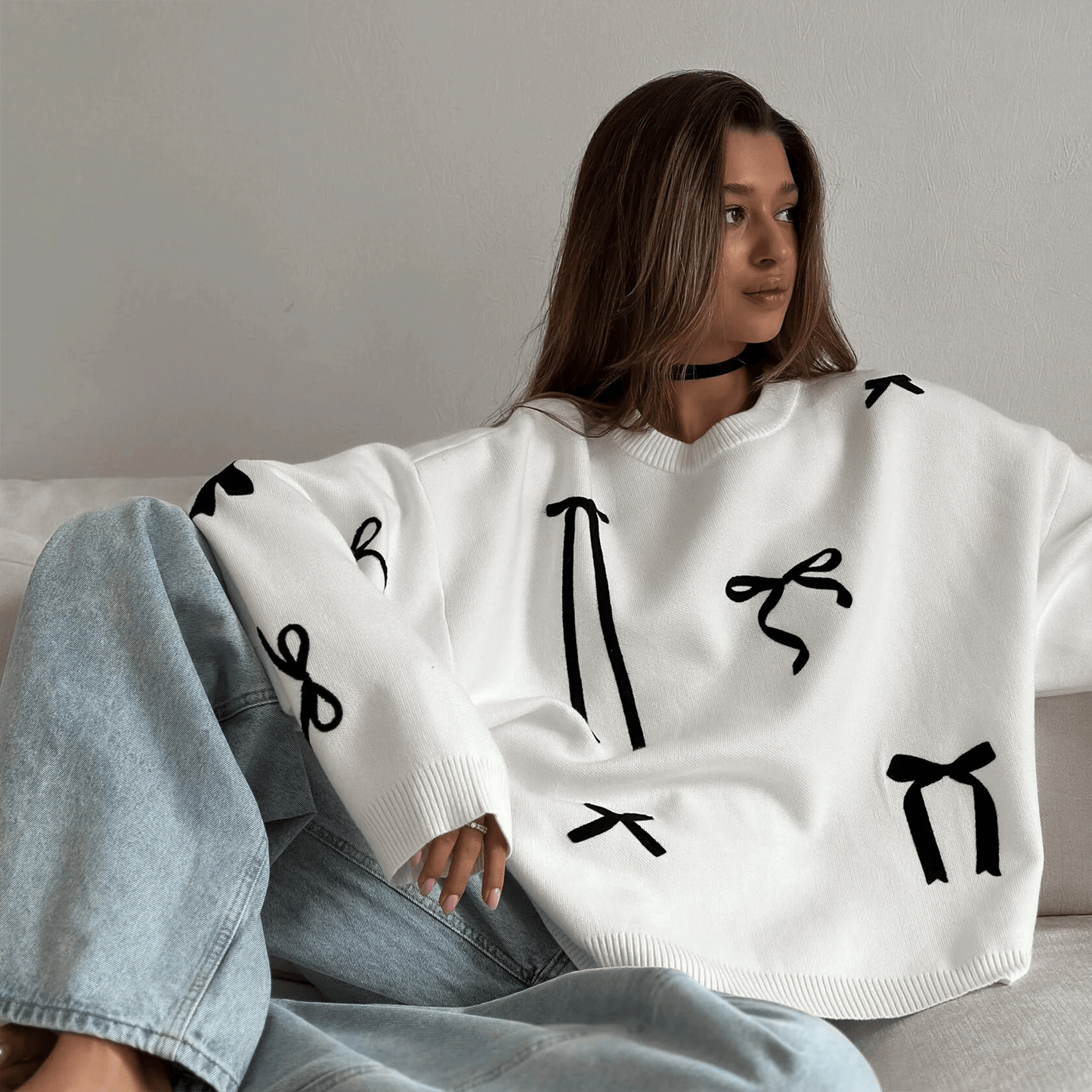 Person wearing a white sweater with black abstract patterns sitting on a couch.