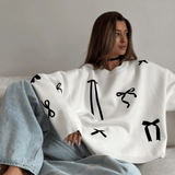 Person wearing a white sweater with black abstract patterns sitting on a couch.