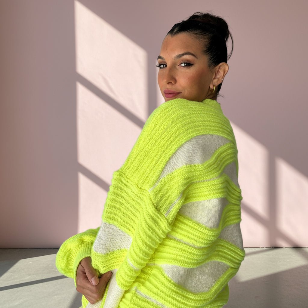 Woman wearing a bright green and white striped sweater against a pink wall.