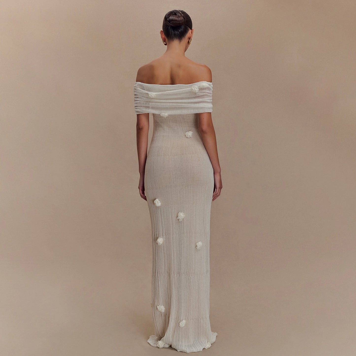 Woman wearing a long, off-shoulder dress with floral details on a beige background