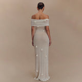 Woman wearing a long, off-shoulder dress with floral details on a beige background