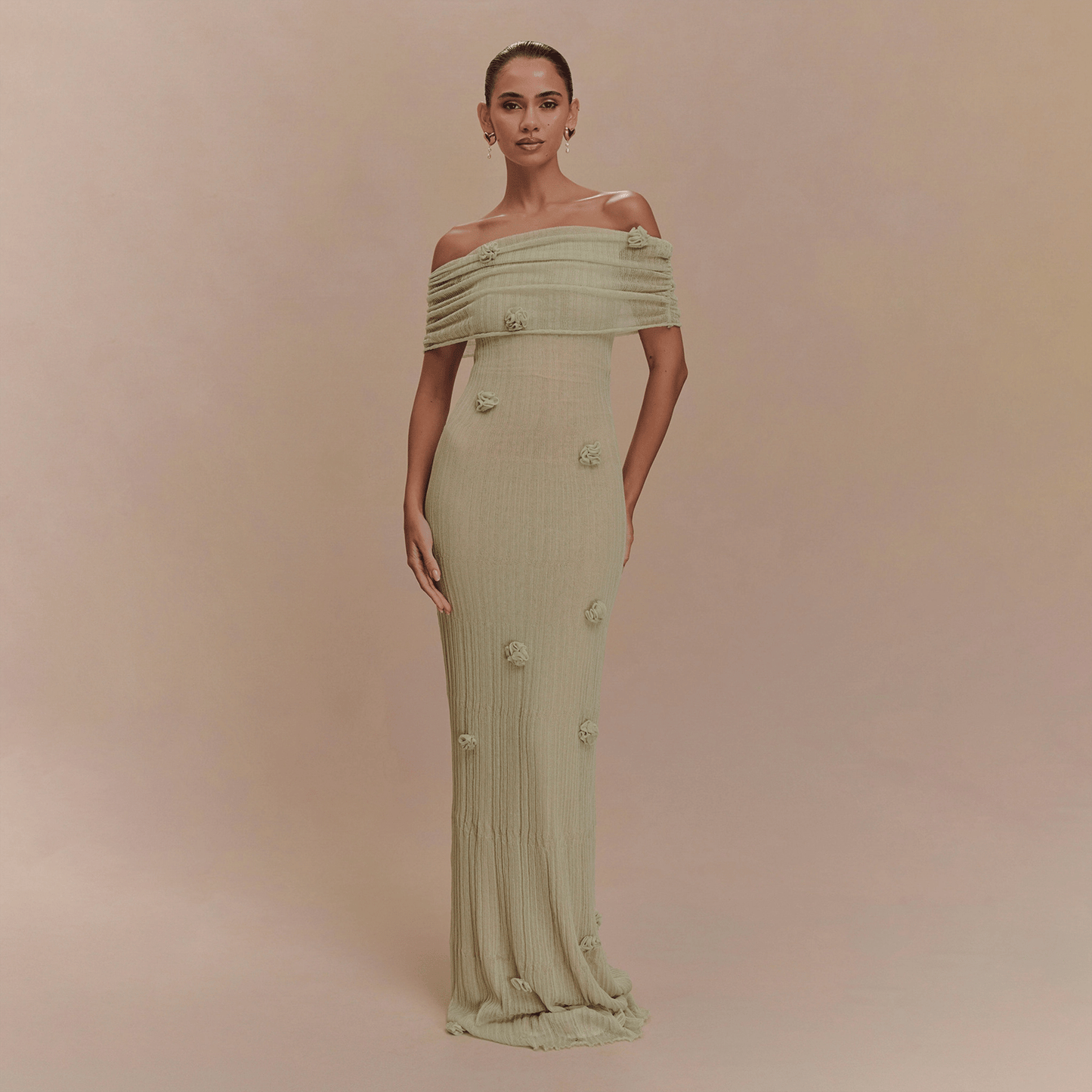 Woman wearing a light green off-shoulder dress with floral details on a beige background