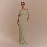 Woman wearing a light green off-shoulder dress with floral details on a beige background