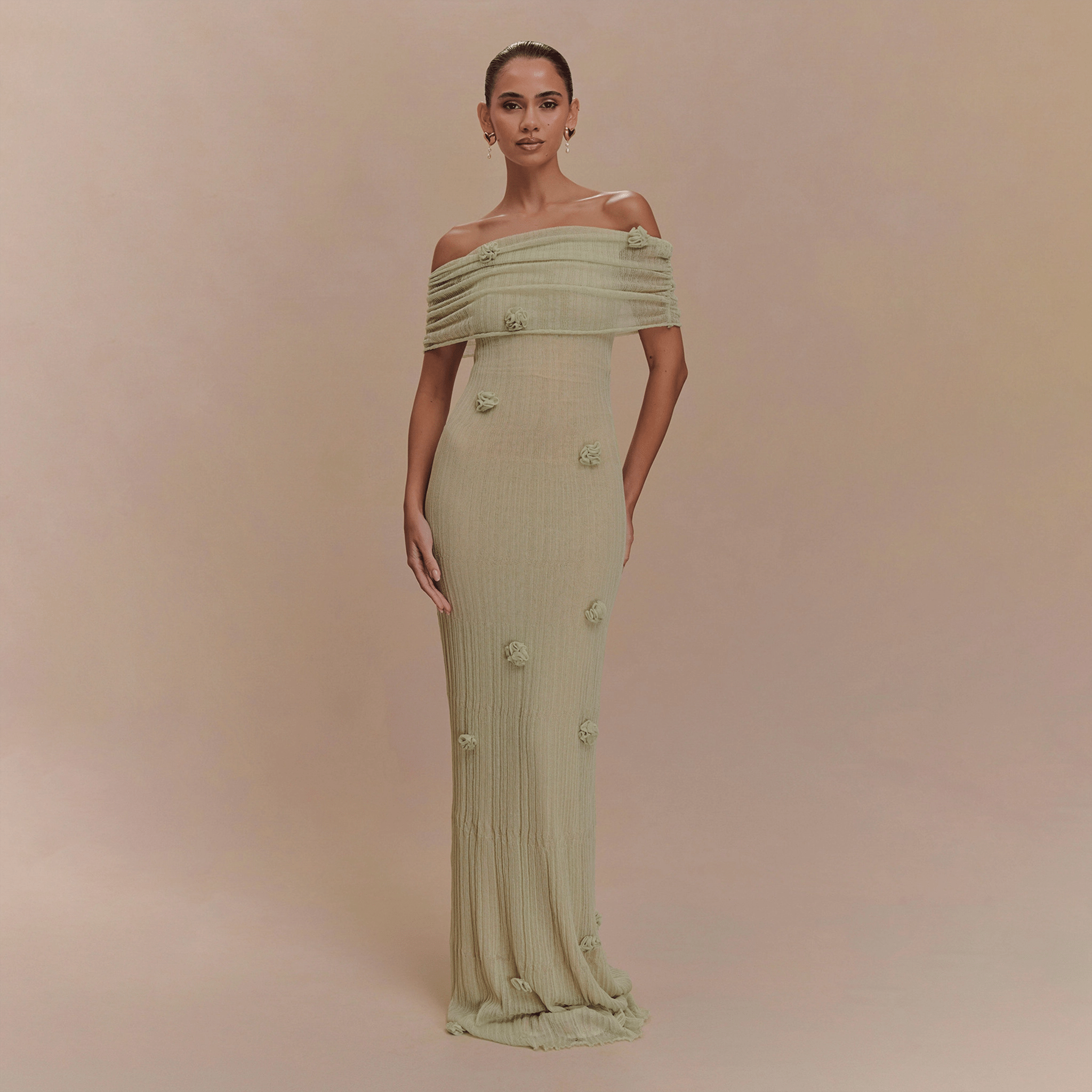 Woman wearing a light green off-shoulder dress with floral details on a beige background