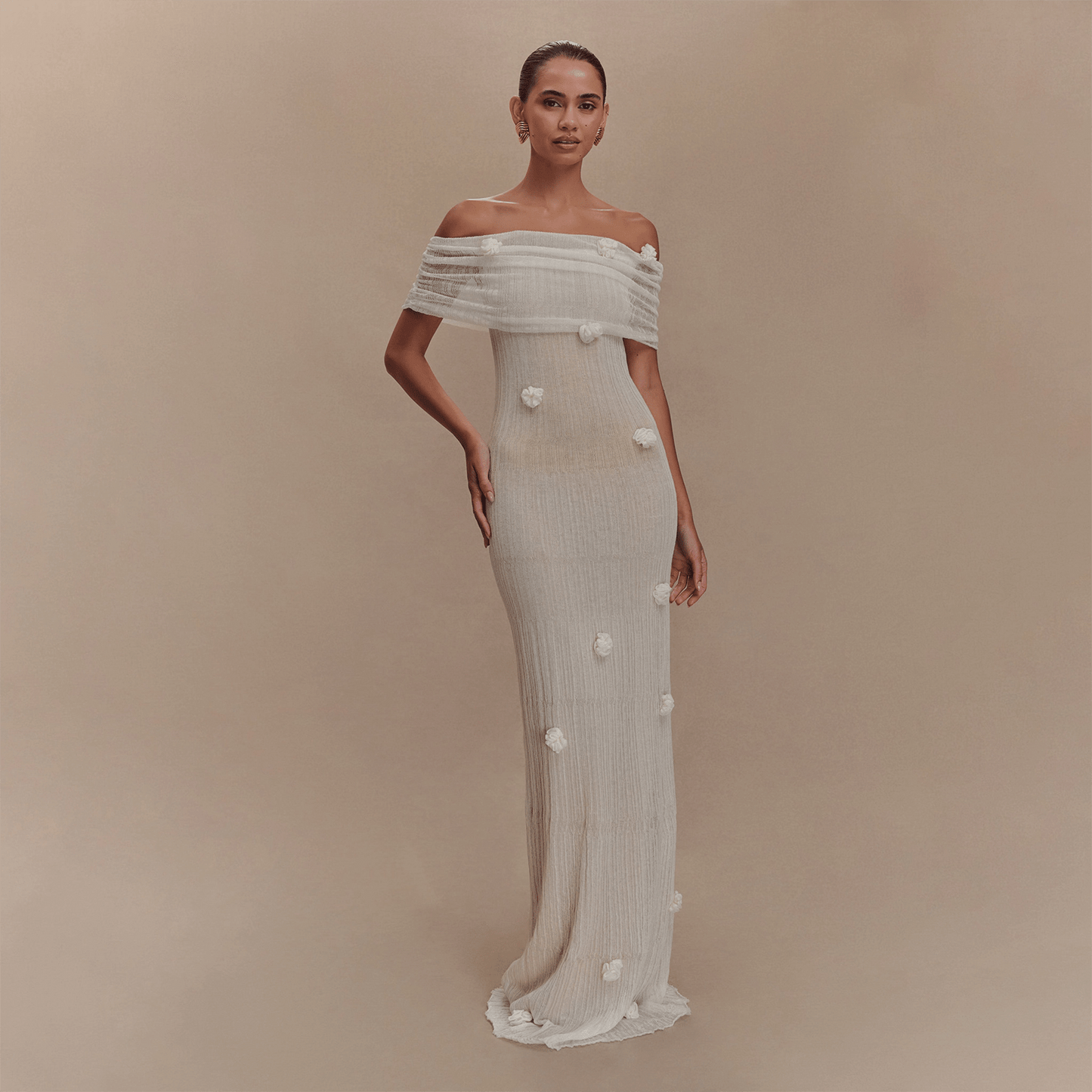 Woman wearing a white off-shoulder gown with floral details on a beige background