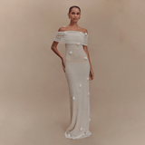 Woman wearing a white off-shoulder gown with floral details on a beige background