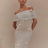 Woman wearing a light-colored off-shoulder dress with floral details against a beige background