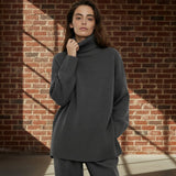 Woman wearing a gray turtleneck sweater against a brick wall