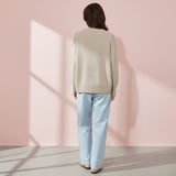 Person wearing a beige sweater and light blue jeans against a pink wall.