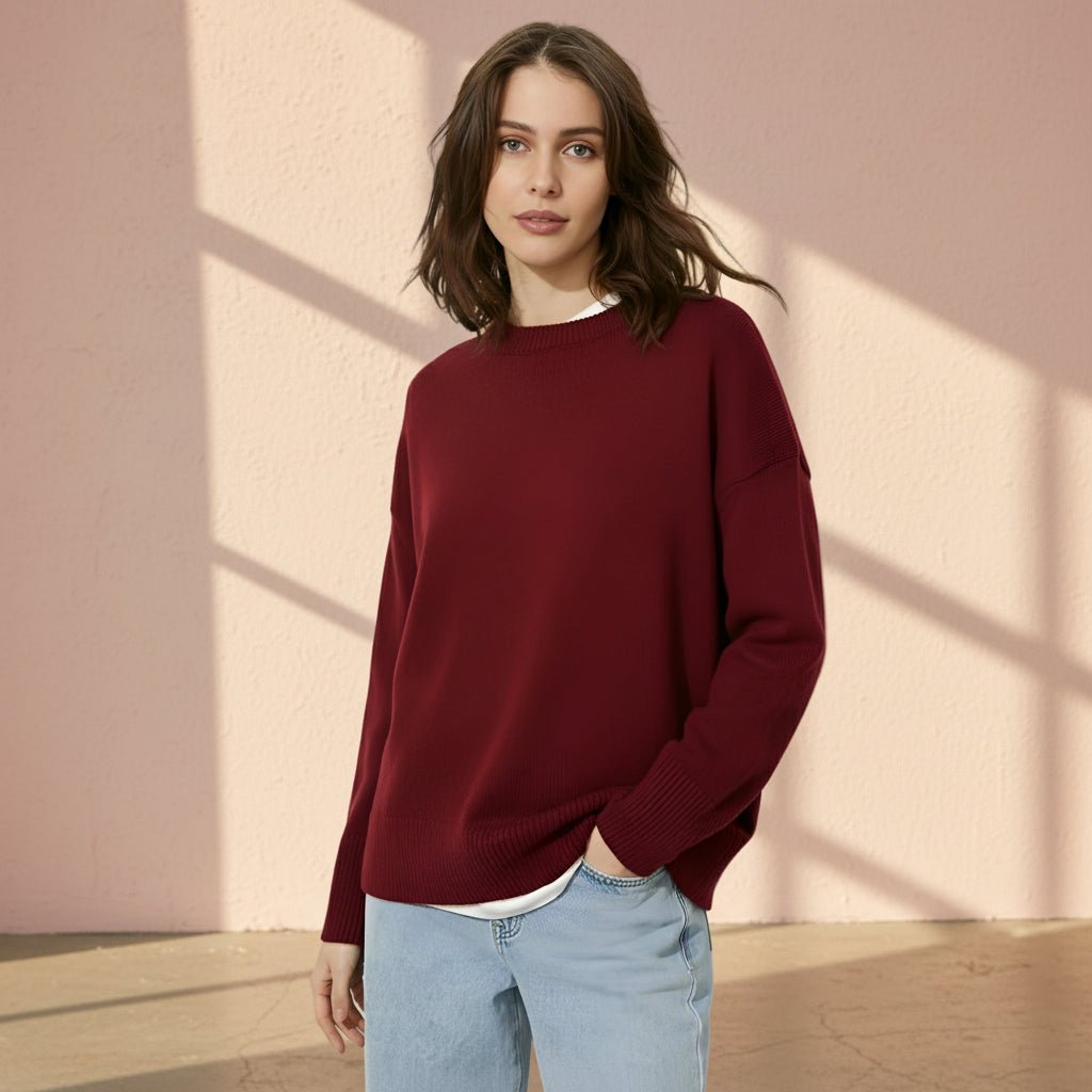 Woman wearing a burgundy sweater and light blue jeans on a gray background