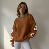 Woman wearing a brown sweatshirt with white lettering against a neutral background