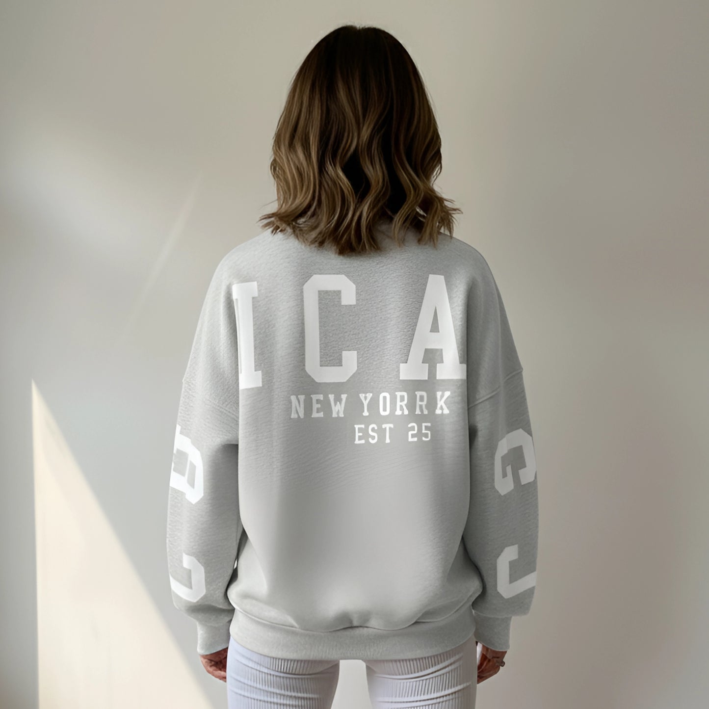 Woman wearing a light gray back side sweatshirt with a brand logo against a neutral background