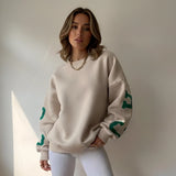 Woman wearing a beige sweatshirt with green patterns against a neutral background