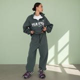 Person wearing a gray 'Palm Spring' tracksuit against a light green wall.