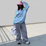 Person wearing a light blue sweatshirt with text and gray pants, holding a white bag on a plain background