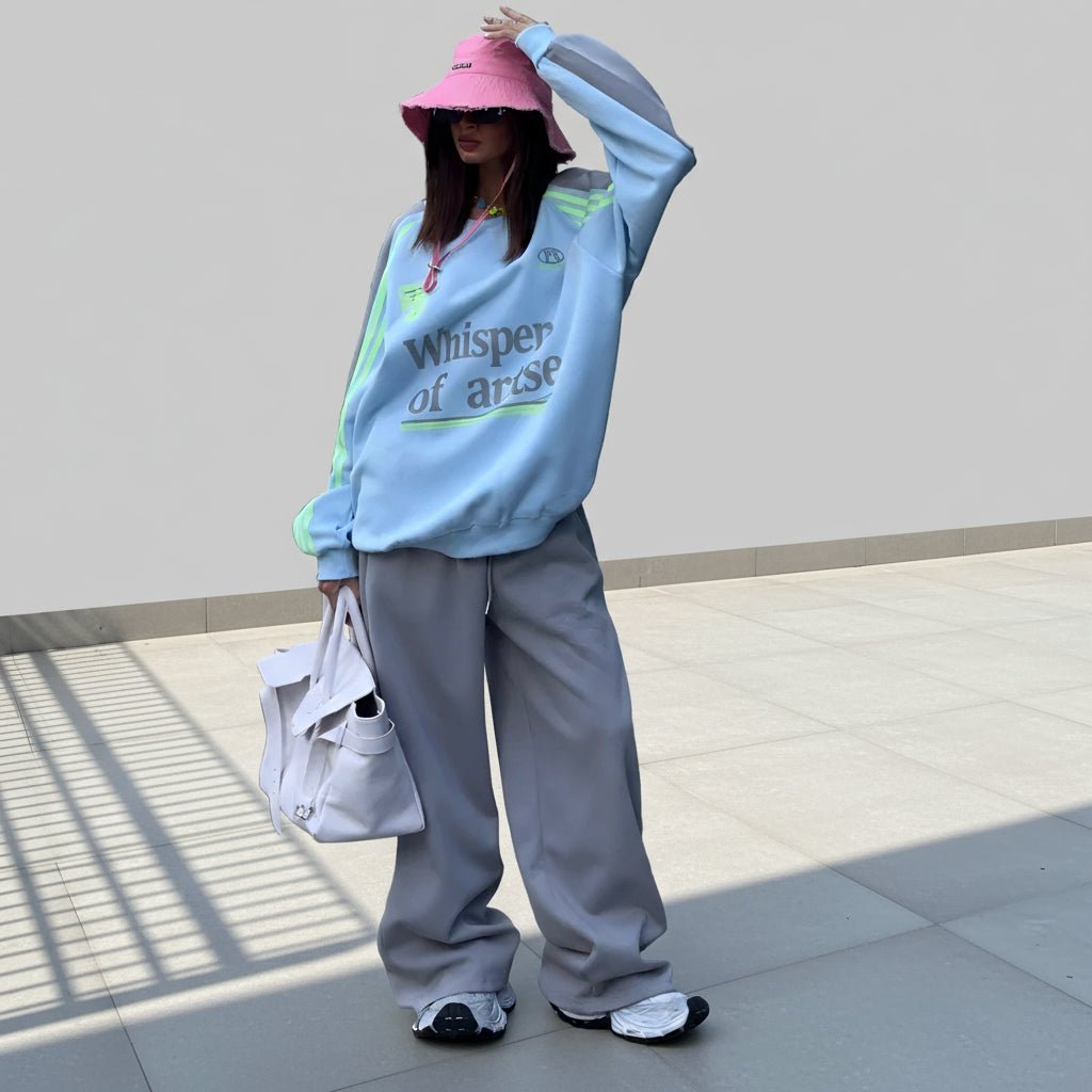 Person wearing a light blue sweatshirt with text and gray pants, holding a white bag on a plain background