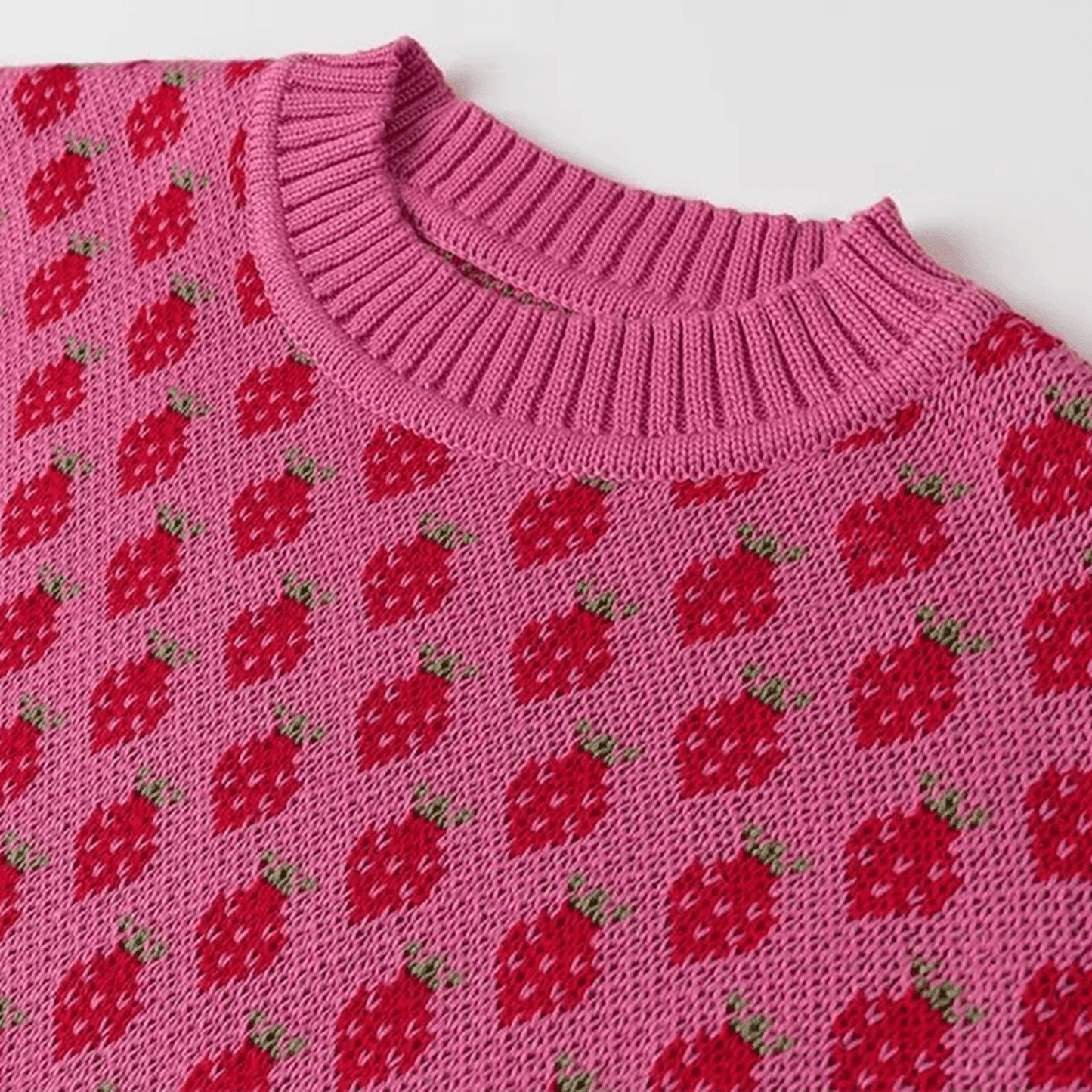 Pink knitted sweater with red strawberry pattern on a white background