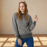 Woman wearing a patterned sweater and blue pants in a well-lit room.