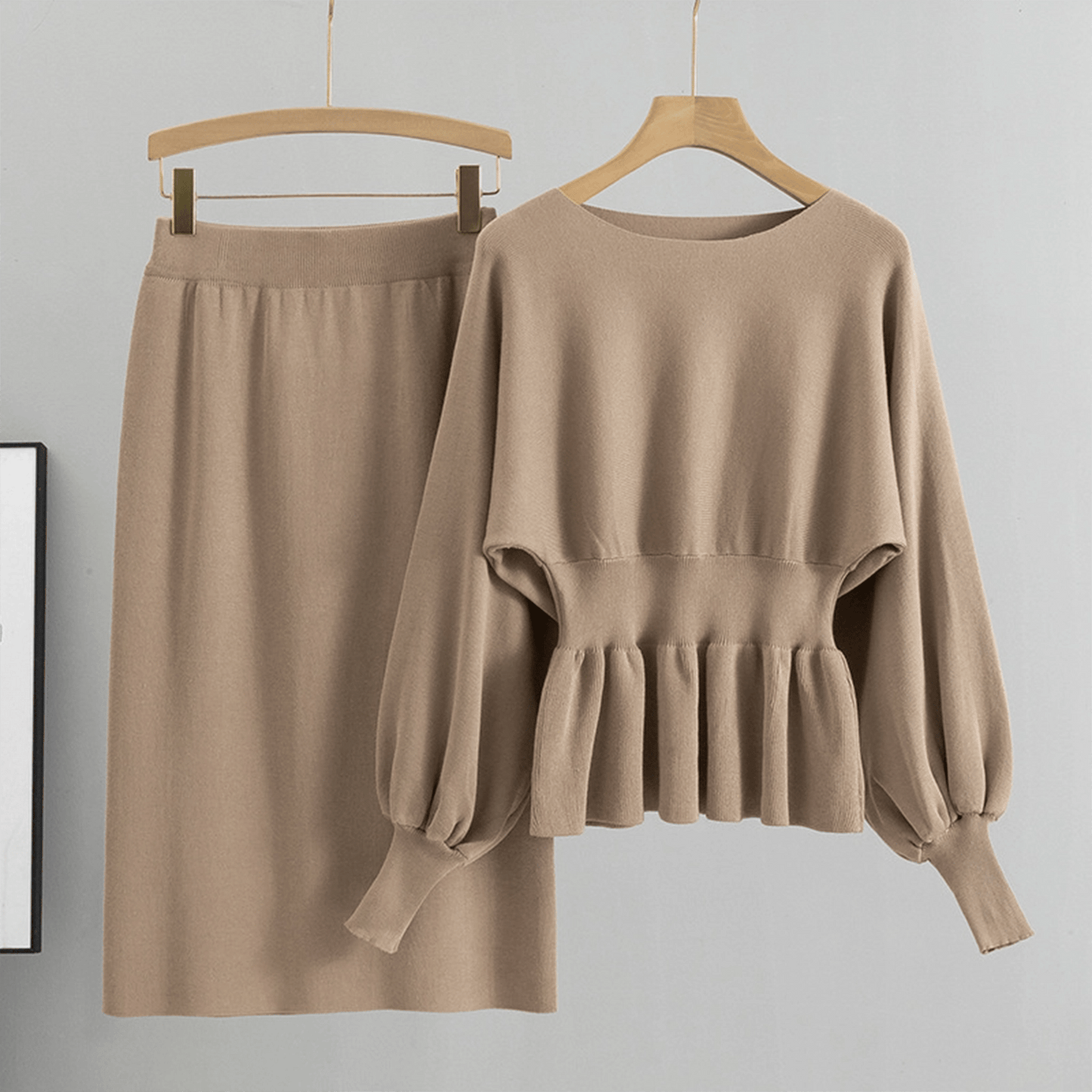 Beige sweater and skirt set on hangers against a gray background