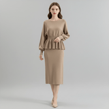 Woman wearing a beige peplum top and skirt on a gray background