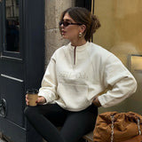 Woman wearing a 'Sunday Club' sweatshirt sitting on a bench with a coffee cup.