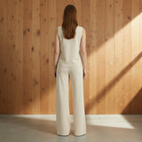 Woman wearing a beige sleeveless top and pants on a gray background